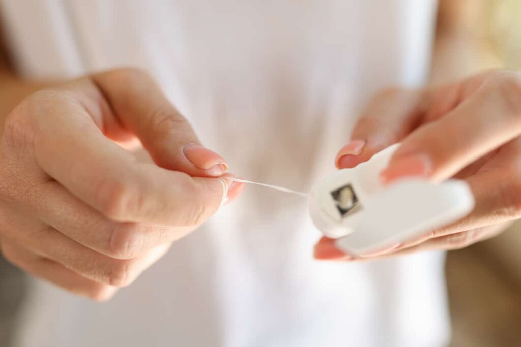 a photo of two hands pulling floss out of the container demonstrating how to hold the floss.