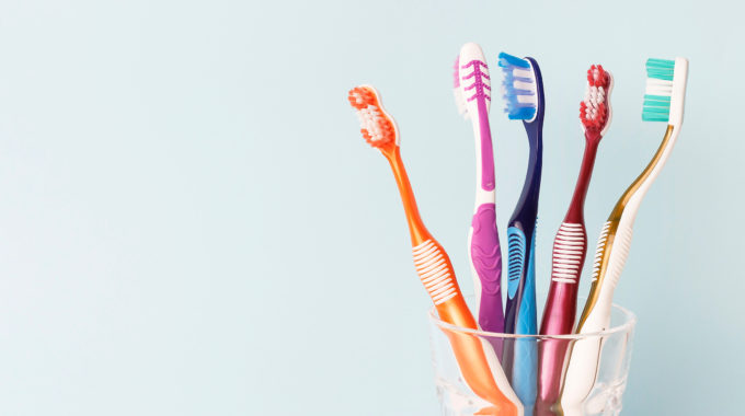 Cup Of Colorful Toothbrushes On A Pale Blue Background