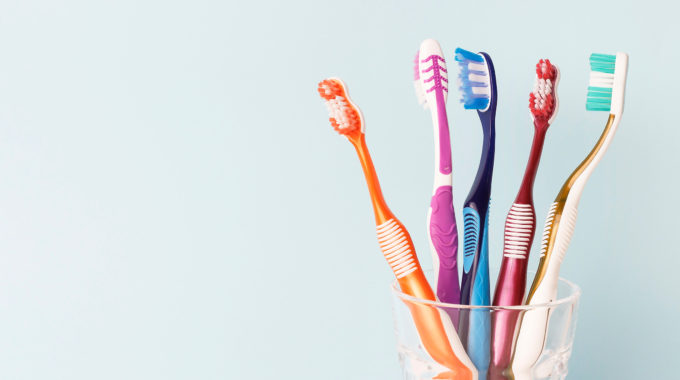 Pleasant St Dental | East Longmeadow, MA | Cup of colorful toothbrushes on a pale blue background