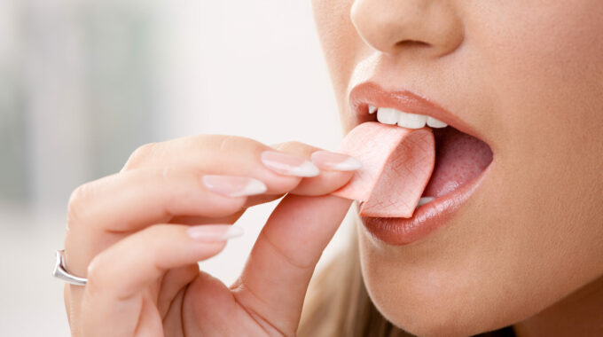 is chewing gum bad for you? this is a woman putting a piece of bubble gum into her mouth.