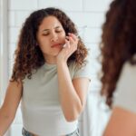 a photo of a woman experiencing mouth pain while brushing her teeth