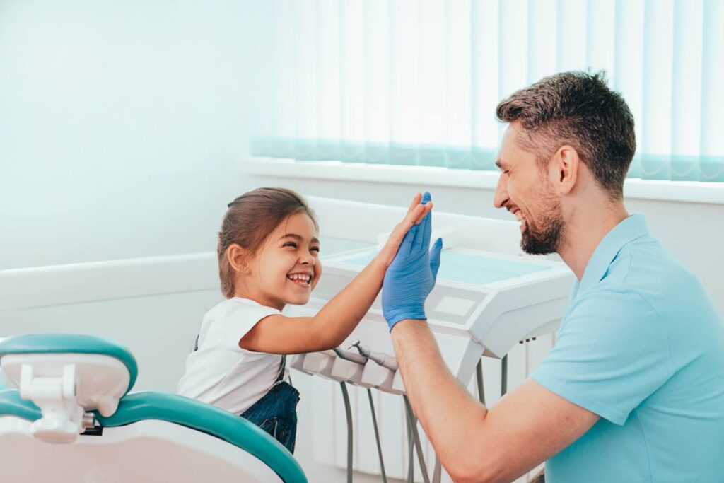 Child not scared of the dentist. Laughing Little girl giving high-five to dentist
