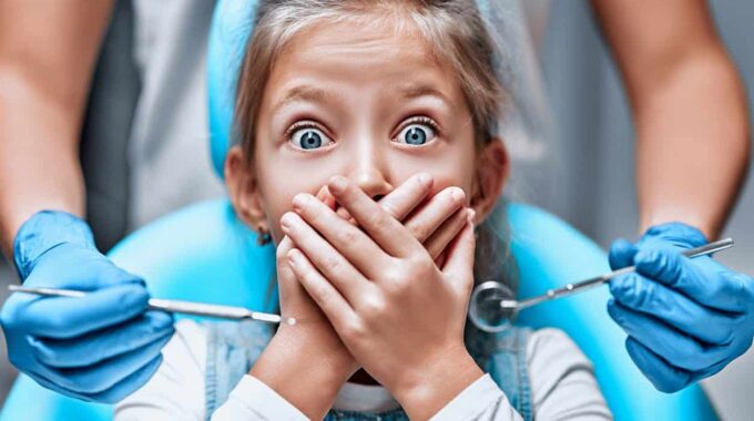 child afraid of the dentist covering her mouth. her parents don't know how to make the dentist less scary for children.