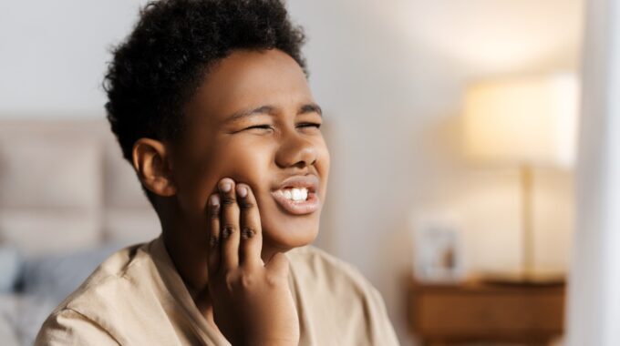 a photo of a little boy touching cheek, feeling severe toothache at home possibly caused by grinding teeth