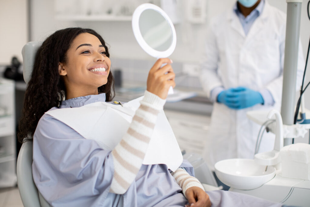 Woman smiling at mirror after dental implant procedure at a Western Massachusetts dental office