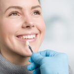 Woman smiling as a dentist holds a porcelain veneer shade sample to her teeth