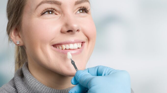 Woman smiling as a dentist holds a porcelain veneer shade sample to her teeth